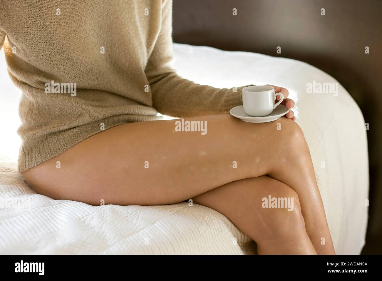 femme dans un pull chameau prenant un café sur le côté du lit, france Banque D'Images