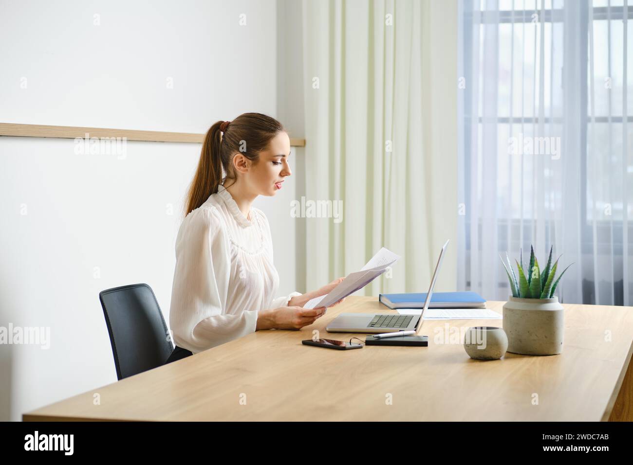 Un agent immobilier professionnel focalisé examine un document papier à son espace de travail propre et organisé dans un bureau lumineux et moderne Banque D'Images