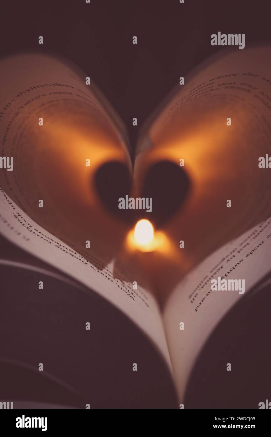 Les pages de livre se sont transformées en un cœur avec une bougie éclairant le centre projetant des ombres sur les mots. Mise en page portrait. Lecture romantique et esthétique moody. Banque D'Images