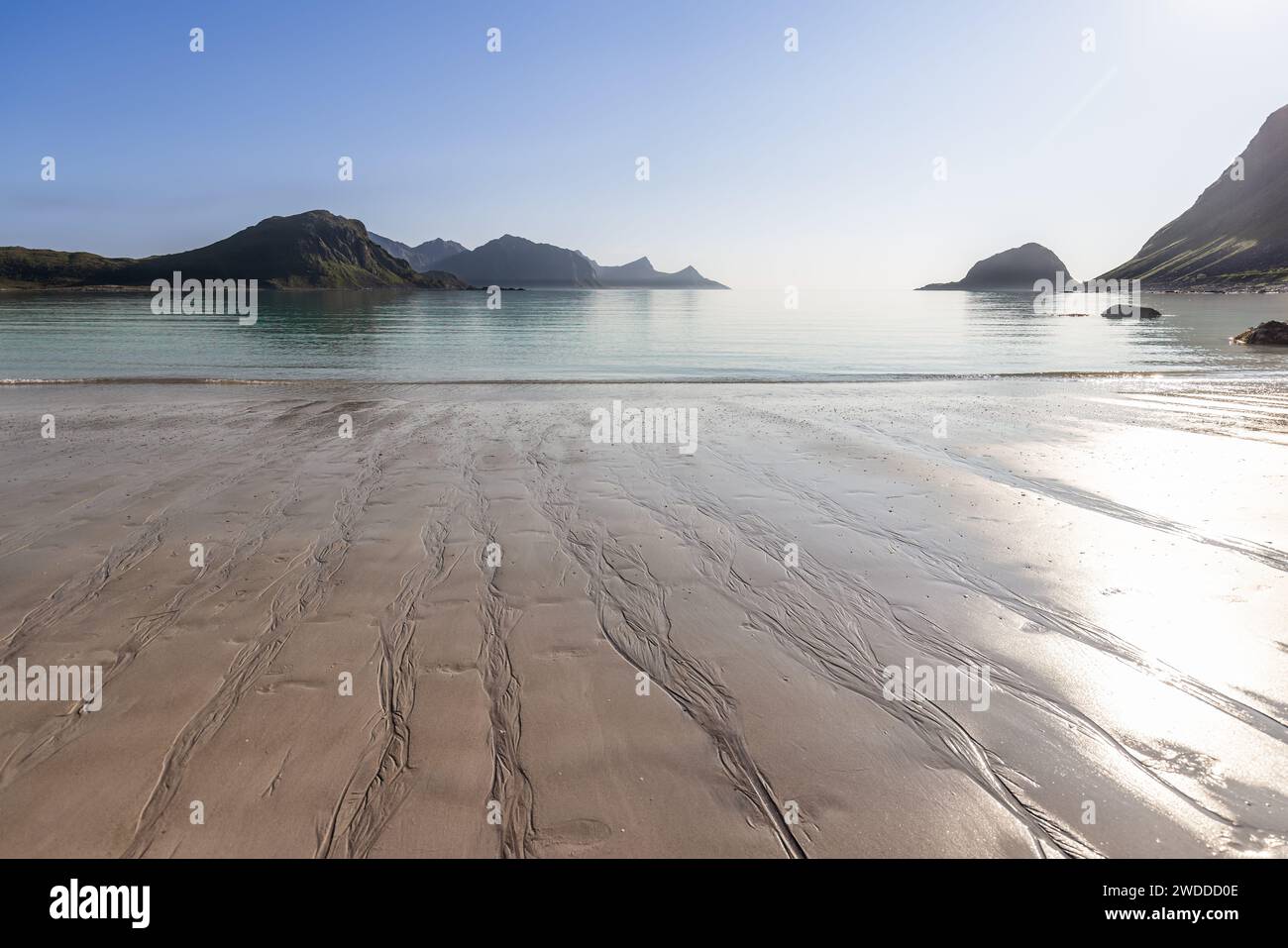 Les motifs de marée gravent le sable de Haukland Beach, Lofoten, Norvège, menant à des eaux tranquilles sous la lueur d'un soleil d'été brillant Banque D'Images