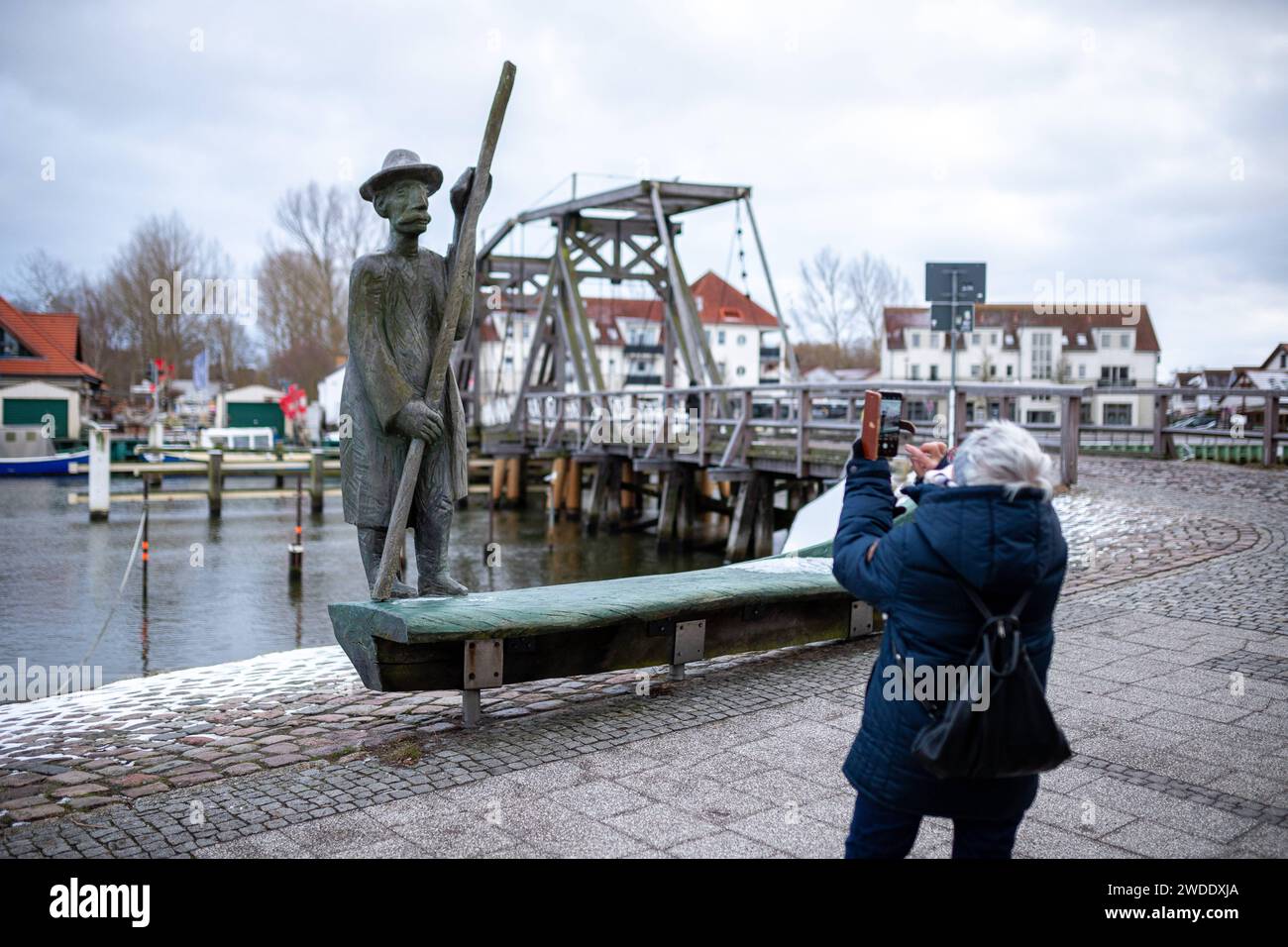 Eine Touristin fotografiert die Holzskulptur eines Fährmanns. Im hintergrund sieht man die historische Klappbrücke Greifswald, Wieck, Ortsteil Wieck, Fischerdorf, Mecklenburg-Vorpommern, MV, Urlaub, Reise, hiver, 2024, Tourismus *** A touriste photographies la sculpture en bois d'un passeur en arrière-plan vous pouvez voir le pont bascule historique Greifswald, Wieck, quartier de Wieck, village de pêcheurs, Mecklenburg-Vorpommern, MV, vacances, voyage, hiver, 2024, tourisme Banque D'Images