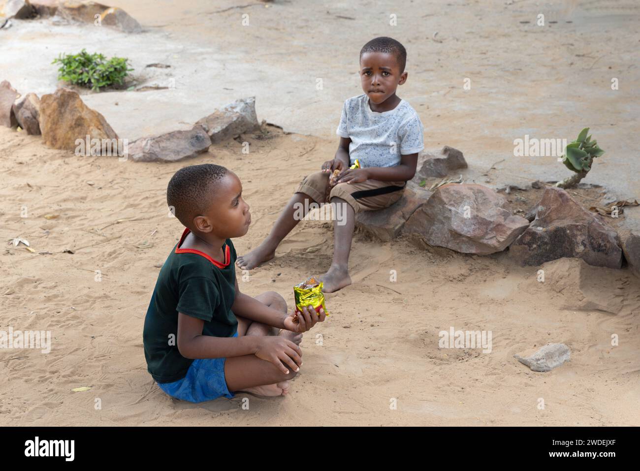 des enfants africains suspendus devant la maison mangeant des collations et des biscuits, attendant sa mère Banque D'Images