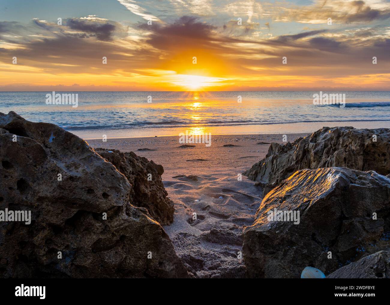 Lever de soleil glorieux avec soleil éclatant entre les rochers sur une plage de sable, idéal pour inspirer le contenu de voyage, décors motivants et décor vibrant. Banque D'Images