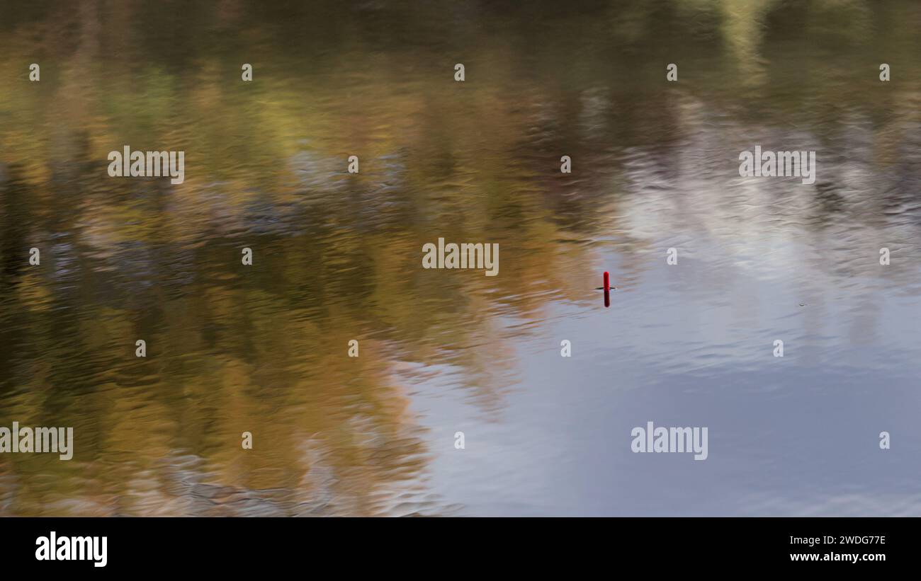 Une photo d'un pêcheur flottant dans un étang de pêche parmi les ondulations et les reflets Banque D'Images