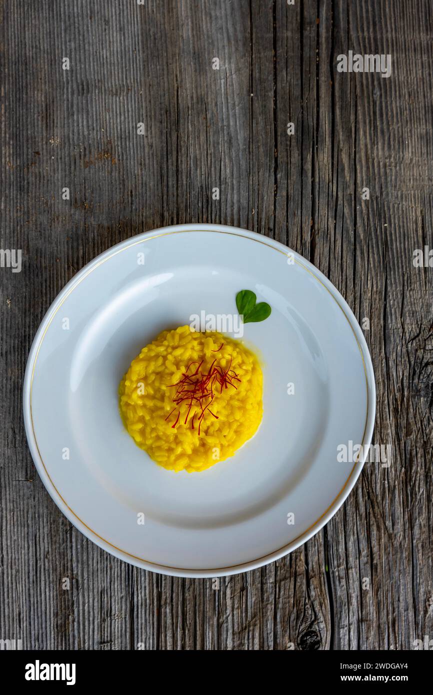 Assiette élégante avec Risotto alla milanais avec safran et parmesan et une feuille en forme de coeur sur une vieille table en bois à Lugano, Tessin, Suisse Banque D'Images