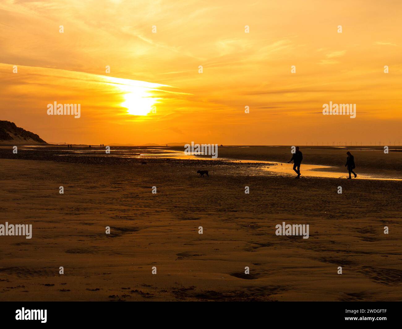 Couple promenant un chien au coucher du soleil sur la plage de Talacre à marée basse, Talacre, Flintshire, pays de Galles Banque D'Images