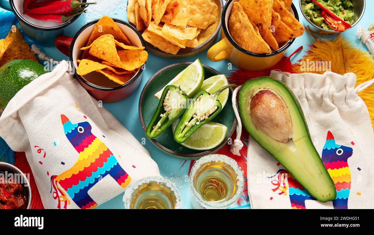Concept Cinco-de-mayo. Nourriture traditionnelle nacho chips sauce salsa tequila Chili avec sel citron vert sombrero serape cactus et maracas sur fond bleu. Banque D'Images