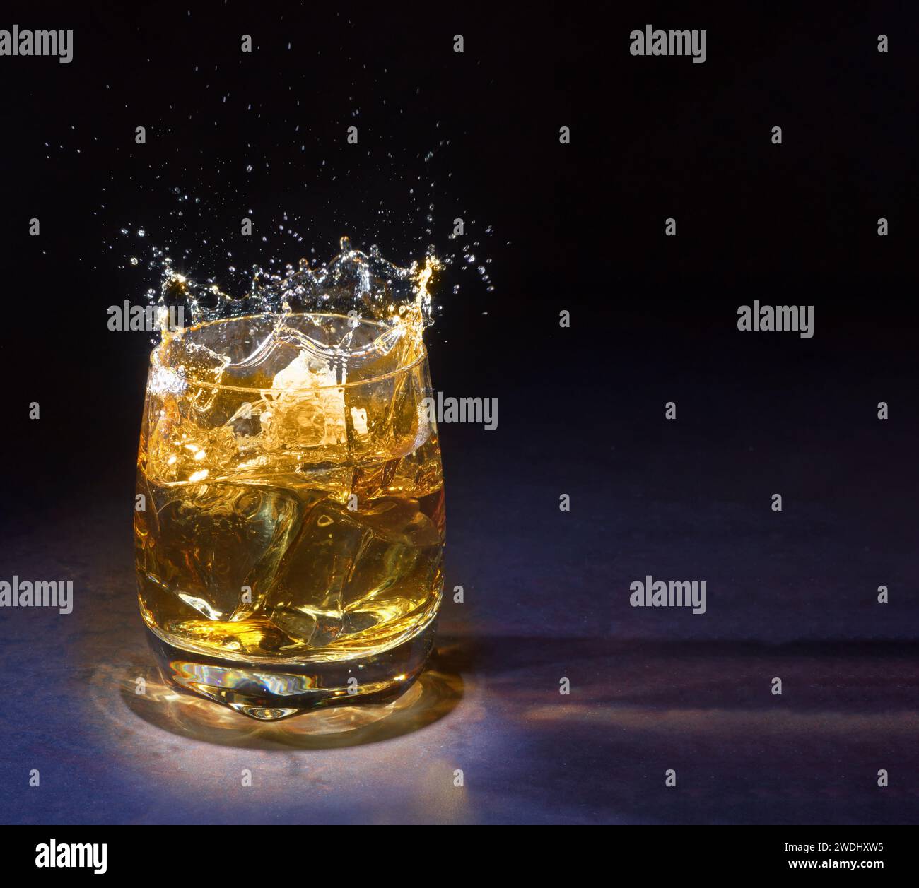 Verre de vieux whisky avec glace. Un verre de whisky éclaboussant avec de la glace isolé sur un fond lumineux Banque D'Images