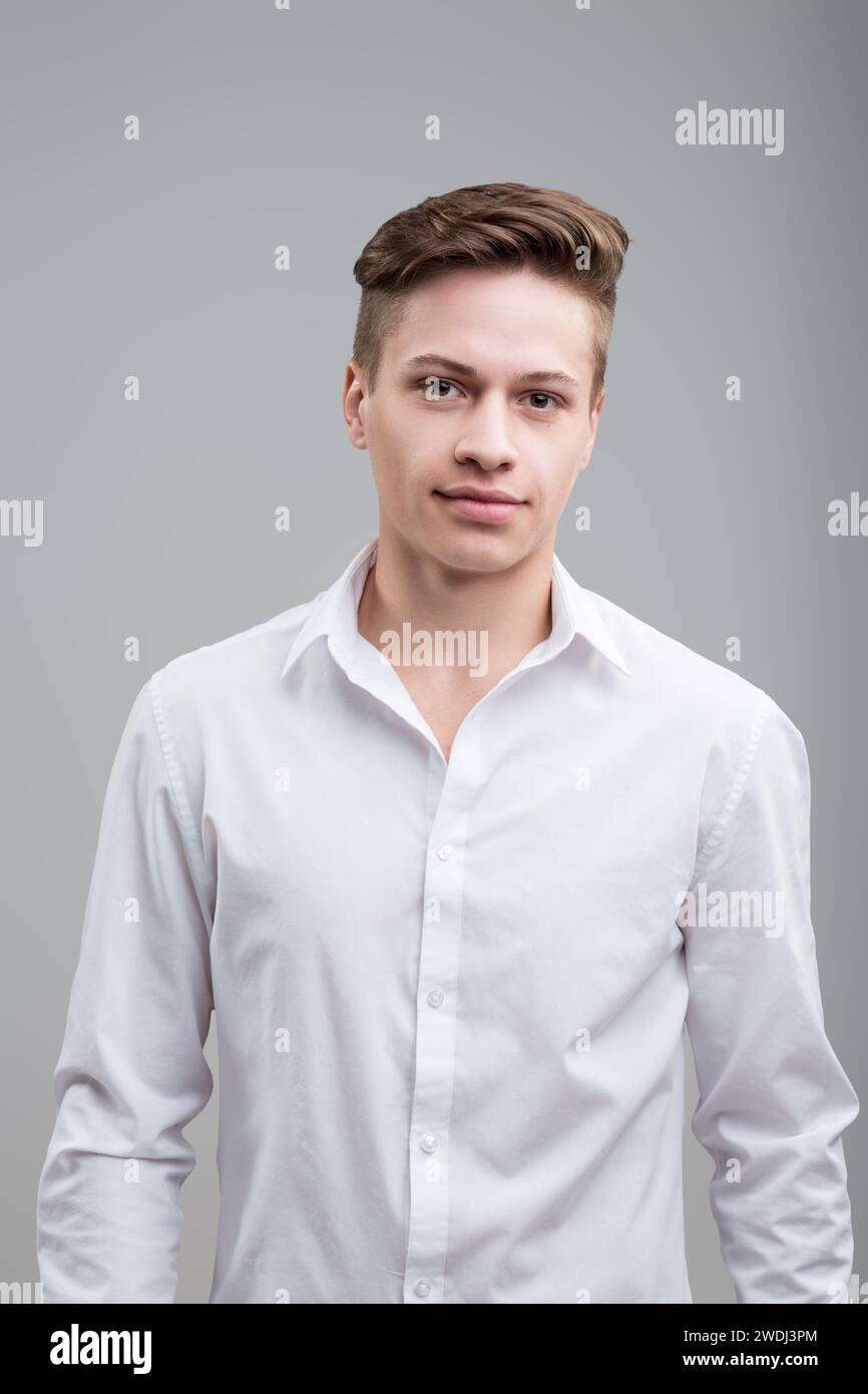 Jeune homme confiant en chemise blanche croustillante, avec un sourire subtil et un regard vif, respire l'accessibilité et le professionnalisme Banque D'Images