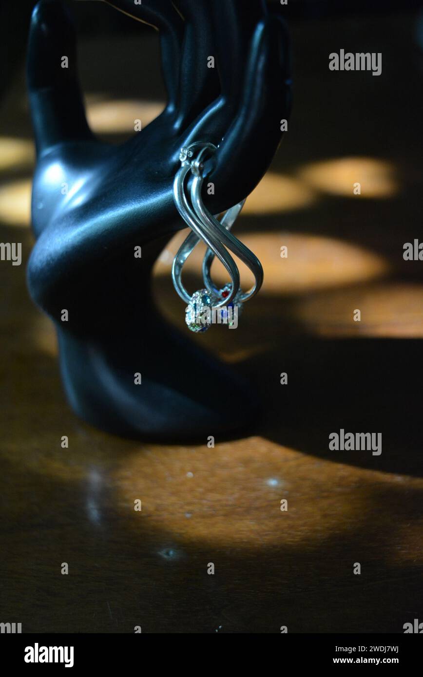 Statuette noire d'une main féminine mate avec boucles d'oreilles en argent avec de belles pierres et un pendentif. Banque D'Images