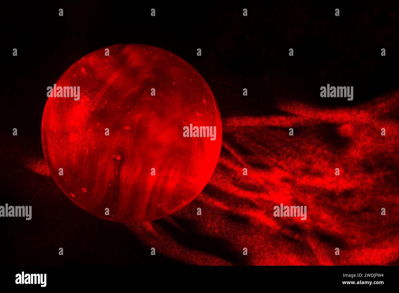 Un marbre de verre rouge sur fond noir peint avec une lumière laser rouge. Banque D'Images