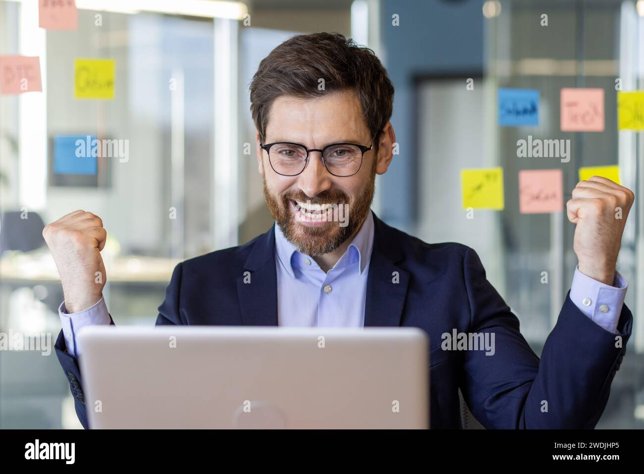 Homme d'affaires gagnant de près à l'intérieur du bureau, homme joyeux célébrant la victoire et les résultats de réussite patron expérimenté mature tenant les mains vers le haut, a reçu notification sur l'ordinateur portable. Banque D'Images