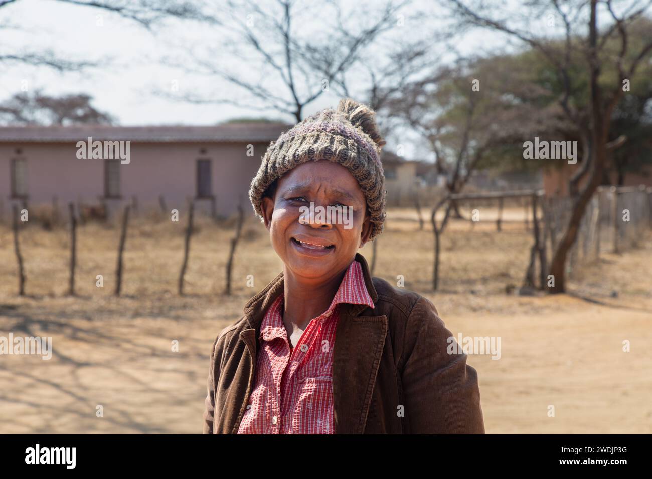 village souriant travailleur social africain femme adulte avec un bonnet marchant sur un chemin de terre Banque D'Images