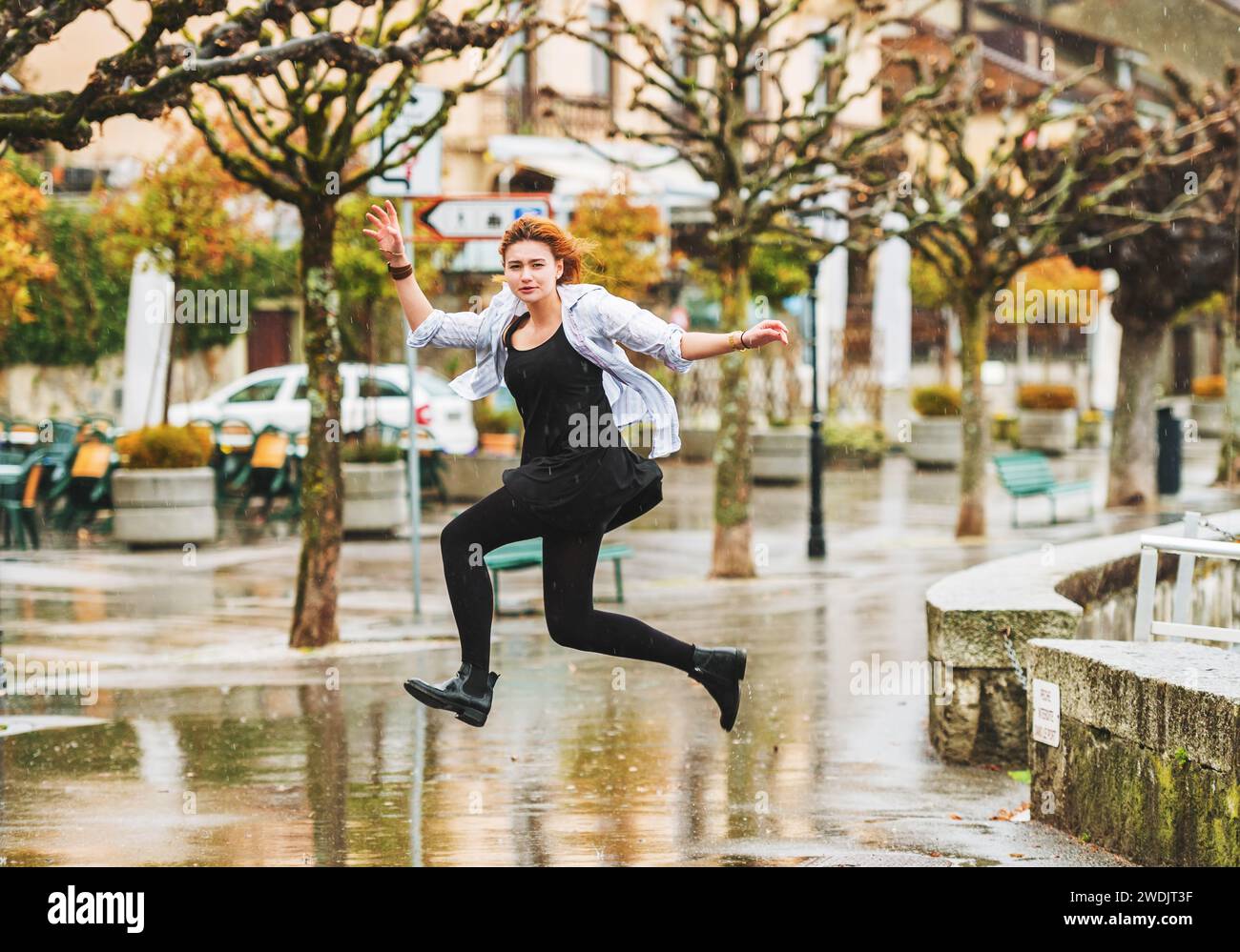 Heureuse jeune fille sous la pluie, sautant par-dessus des flaques d'eau Banque D'Images