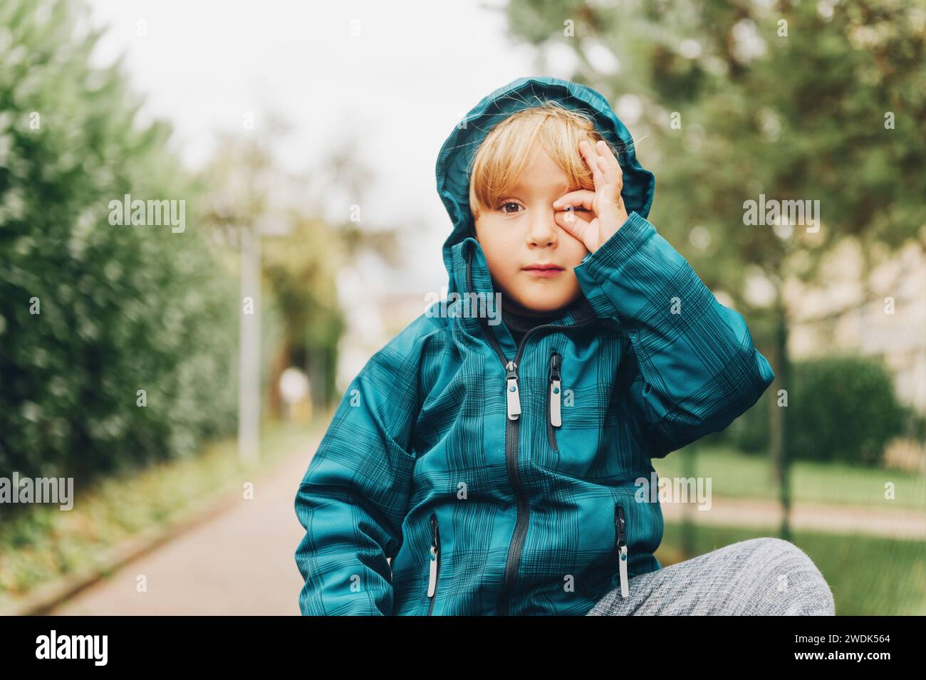 Portrait en plein air de mignon petit garçon prétendant prendre des photos avec sa main, enfant portant une veste bleue imperméable chaude Banque D'Images