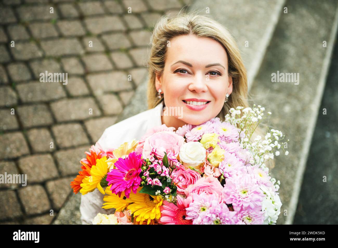 Portrait rapproché extérieur de femme blonde tenant grand bouquet de belles fleurs fraîches Banque D'Images