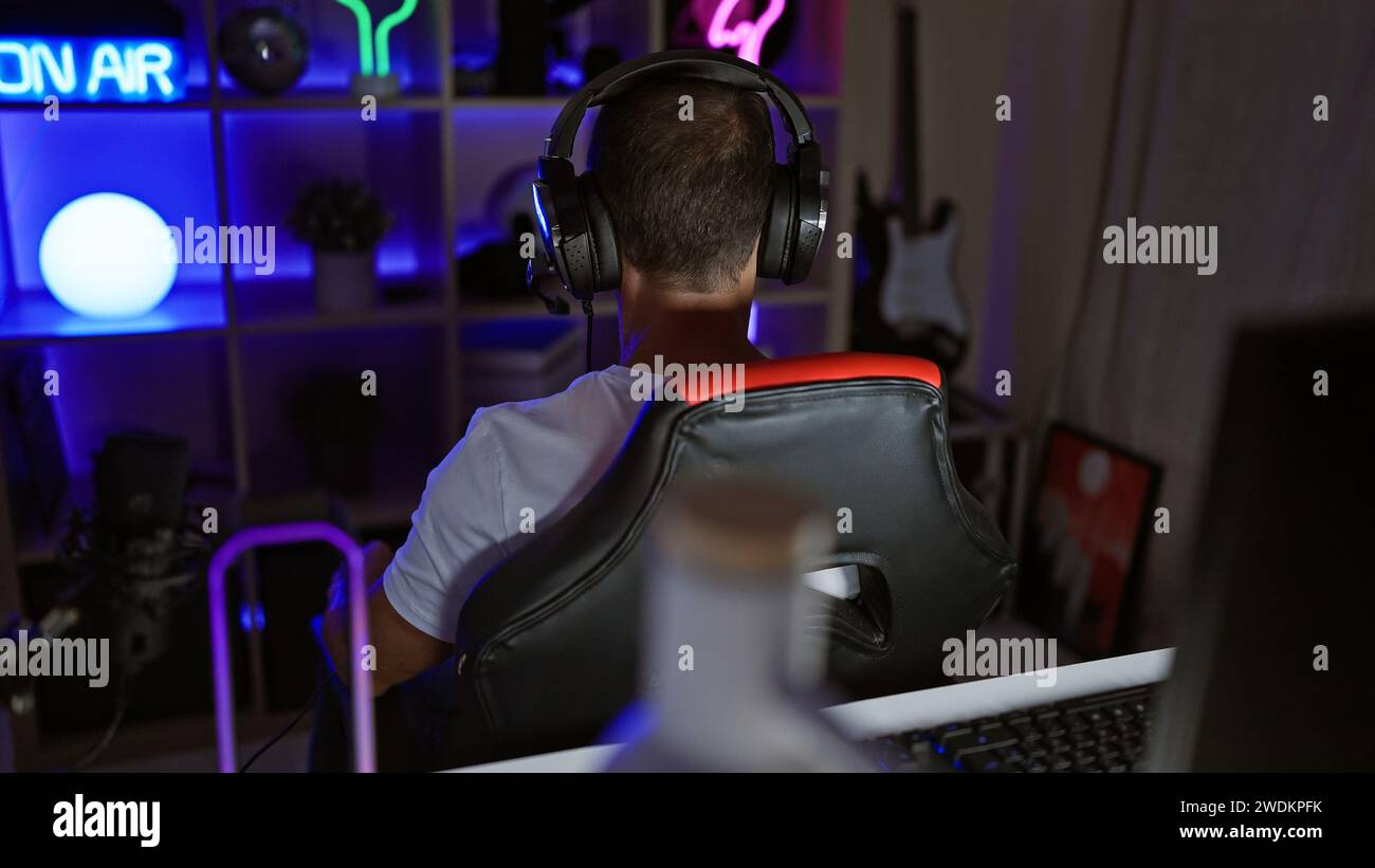 Beau gamer homme d'âge moyen diffuse tard dans la nuit, assis dans sa salle de jeux futuriste, adulte passionné de cyber-technologie engagé dans virtuel Banque D'Images