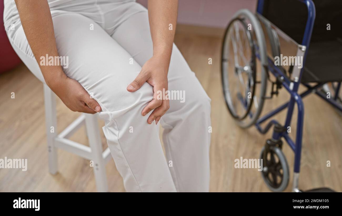Une personne en pantalon blanc est assise près d'un fauteuil roulant dans une clinique de réadaptation, ce qui implique un rétablissement après une blessure ou une intervention chirurgicale. Banque D'Images