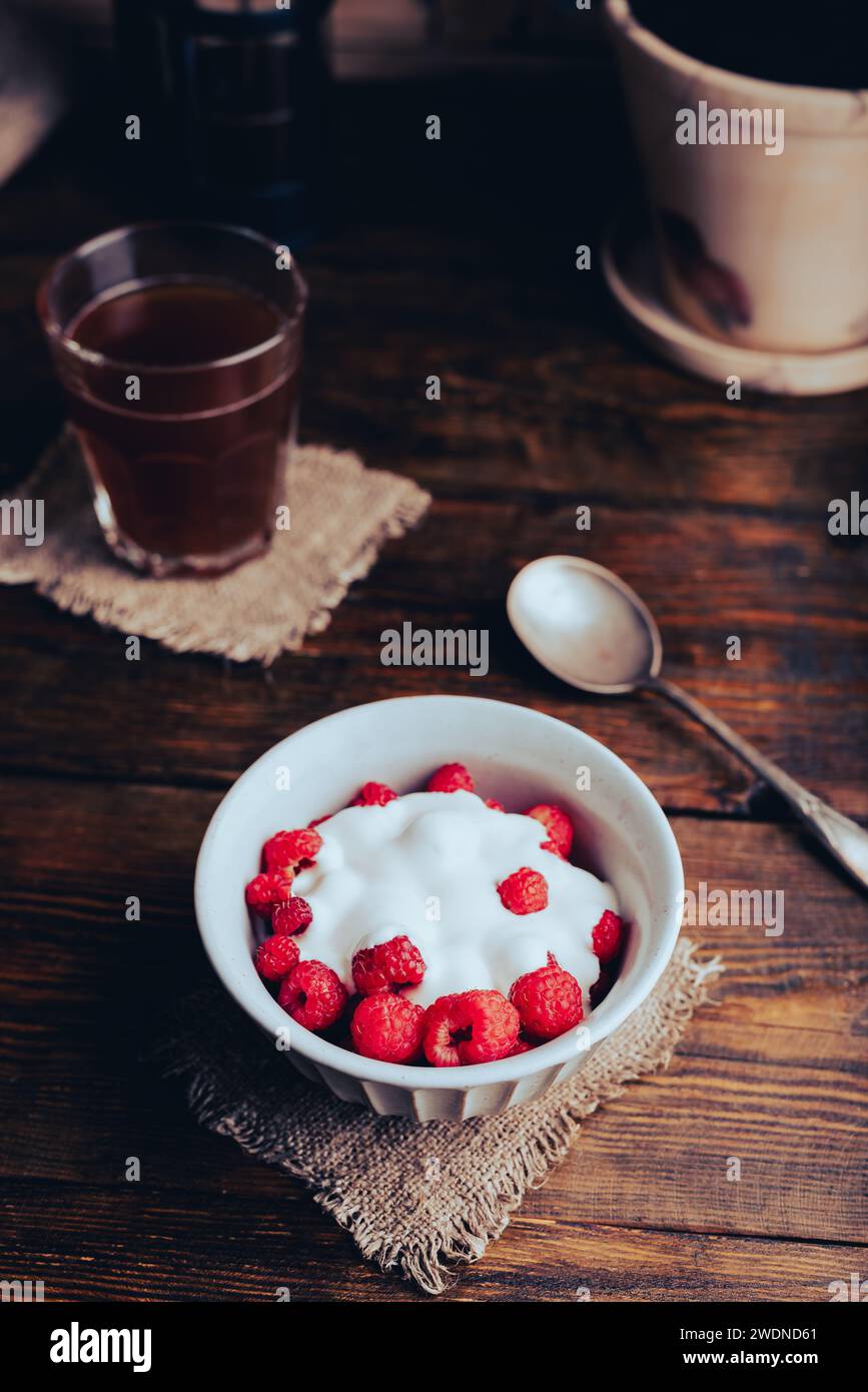 Dessert sain avec framboise mûre et crème dans un bol et un verre de café sur une table rustique Banque D'Images