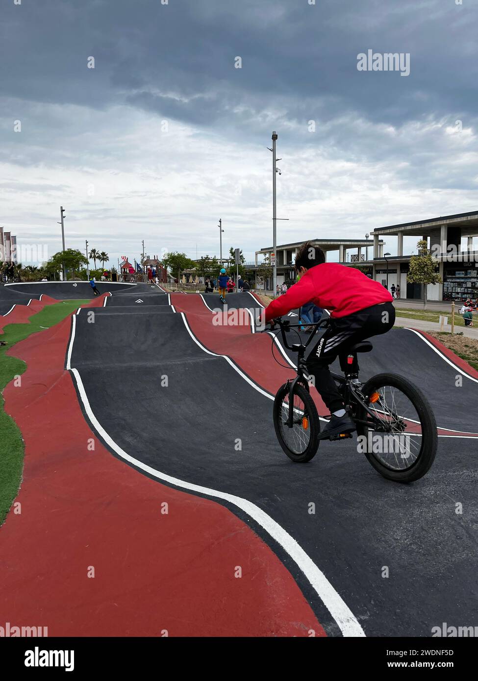 Style Pumptrack : garçon en chemise rouge, chevauchant un vélo noir avec flair sur le circuit urbain dynamique Banque D'Images