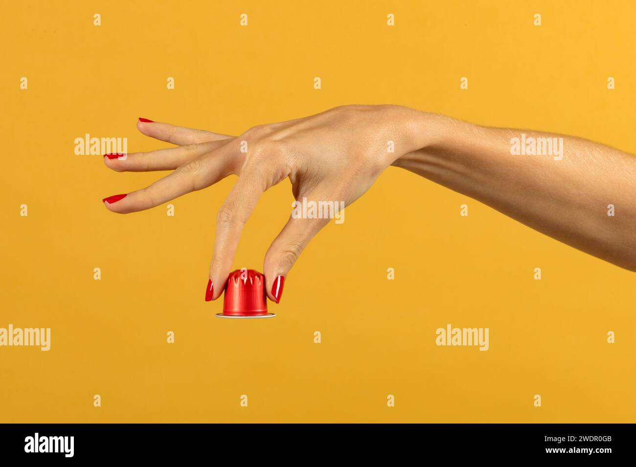 Recadrez la main féminine anonyme avec des ongles peints montrant la capsule de café rouge à l'envers sur fond jaune en studio Banque D'Images