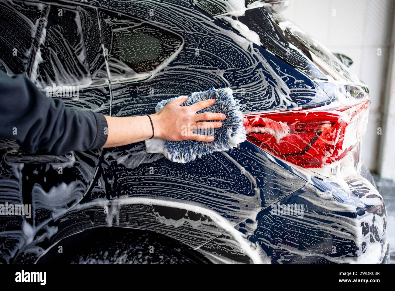 Lavage de voiture professionnel. Le travailleur lave la carrosserie du véhicule avec de la mousse. Photo de stock Banque D'Images