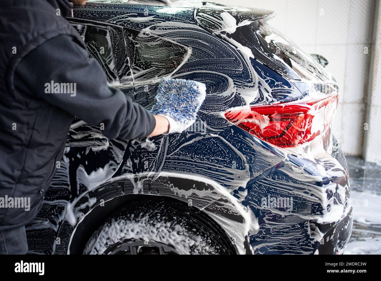 Lavage de voiture professionnel. Le travailleur lave la carrosserie du véhicule avec de la mousse. Photo de stock Banque D'Images