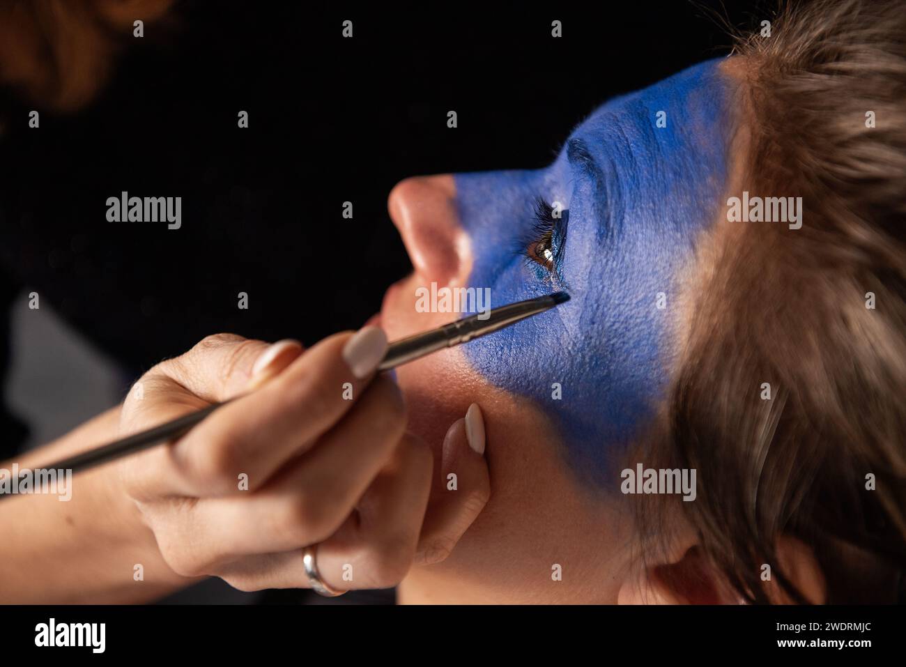 Portrait rapproché d'une femme ayant son visage peint en bleu par un artiste au pinceau. Maquillage créatif, maquillage de performance Banque D'Images