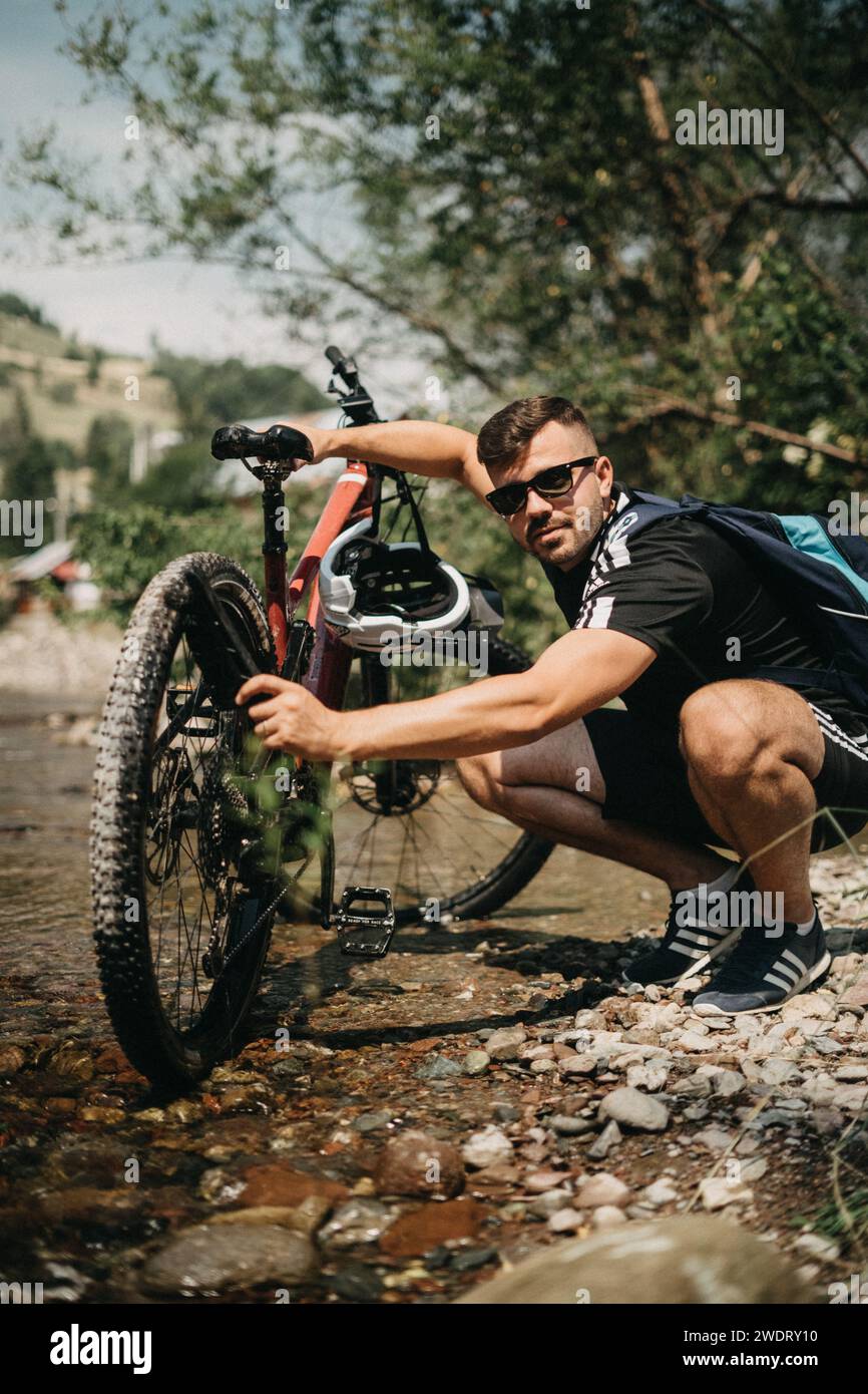 Jeune athlète appréciant laver son vélo électrique dans la rivière Banque D'Images