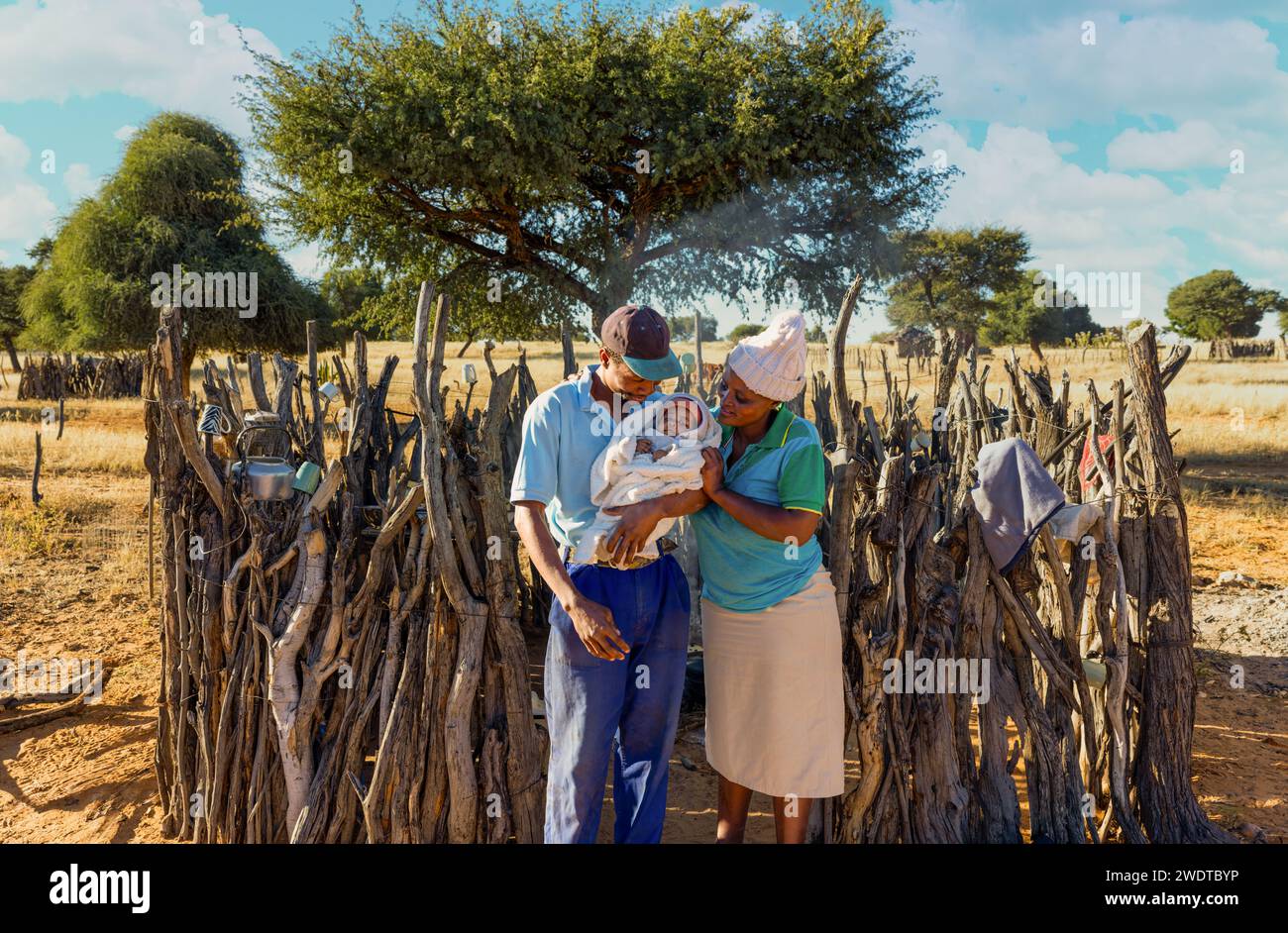 Joyeux parents africains tenant leur nouveau-né, cuisine en plein air dans le village de fond au Botswana Banque D'Images