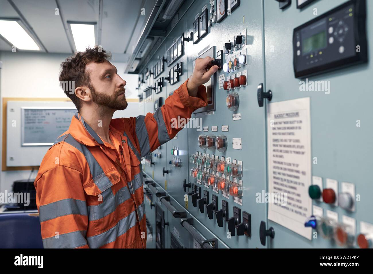 Jeune ingénieur maritime surveillant le travail des équipements électriques dans la salle de contrôle des moteurs. Banque D'Images