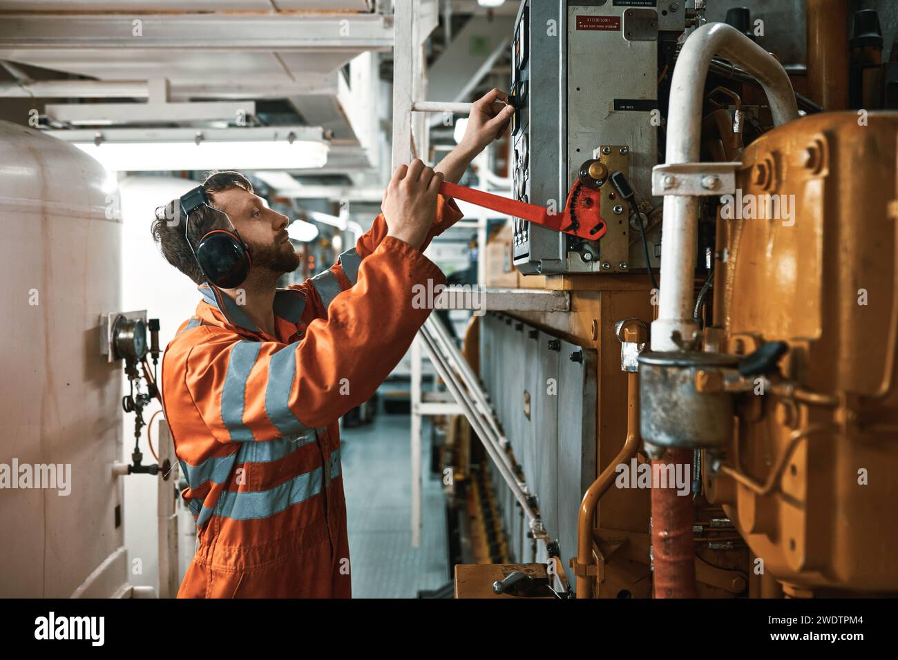 Jeune officier mécanicien dans la salle des machines, portant un équipement de protection individuelle, démarrant manuellement le moteur diesel principal. Banque D'Images