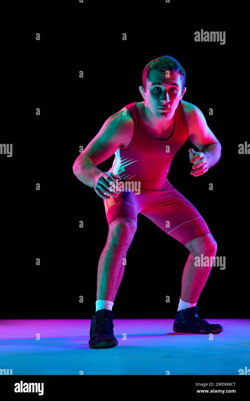 Jeune homme, combattant freestyle professionnel se tient dans la pose d'attaque et regardant la caméra sur fond noir dans des lumières de néon mixtes. Banque D'Images