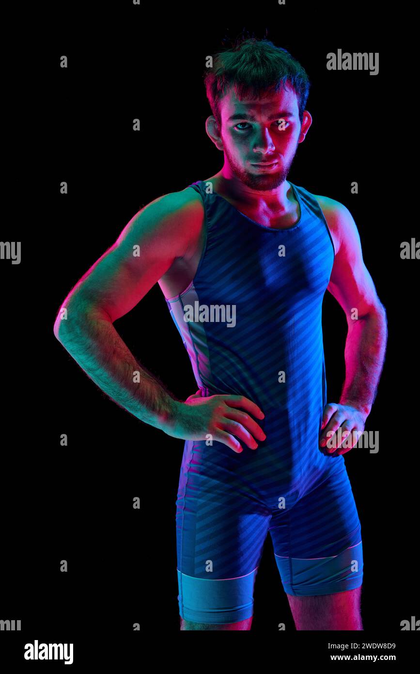 Lutteur freestyle concentré et compétitif en sportwear bleu moderne a mis ses mains sur les hanches et regardant la caméra sur fond noir en néon mélangé Banque D'Images