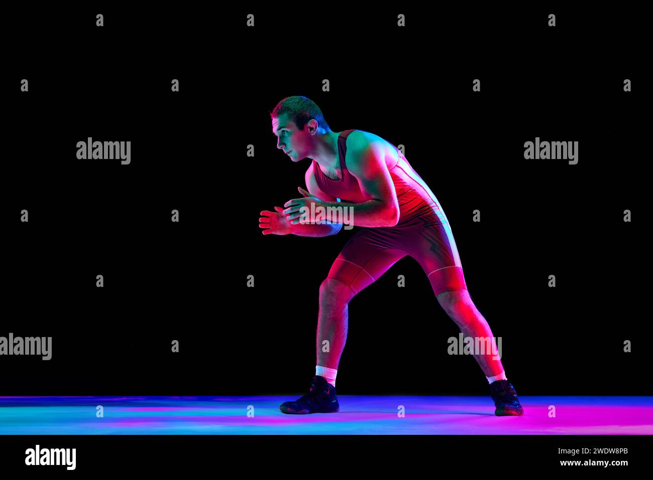 Catcheur freestyle en collants de combat rouges se tient en position d'attaque et regardant ta caméra sur fond noir dans des lumières de néon mixtes. Banque D'Images