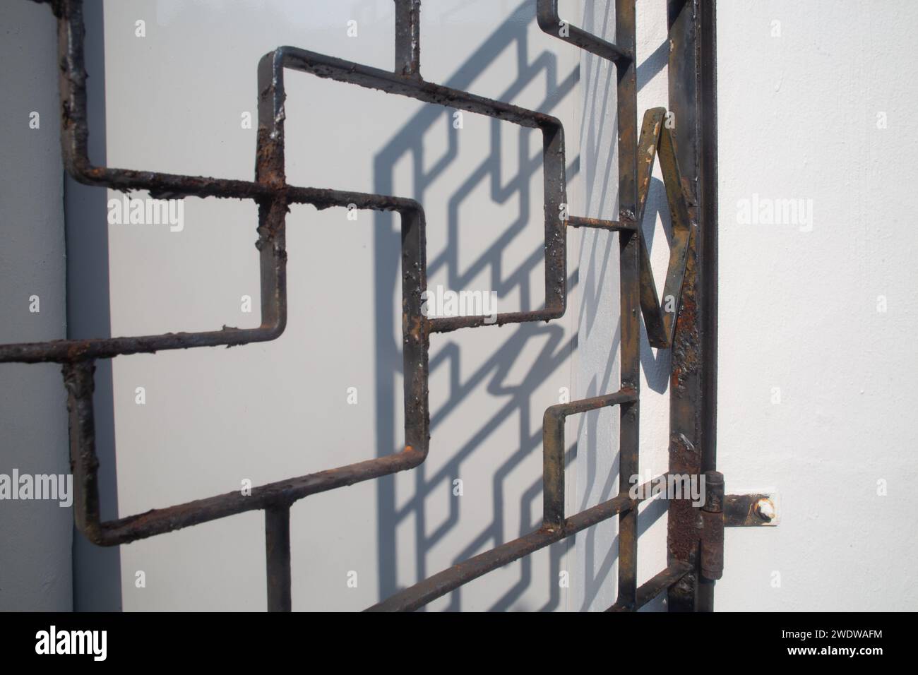 Grille de fer de fenêtre rustique contre le mur blanc, ombre sur le fond blanc pour voir le design. La couche de peinture se décolle et présente de la rouille. Singapour. Banque D'Images