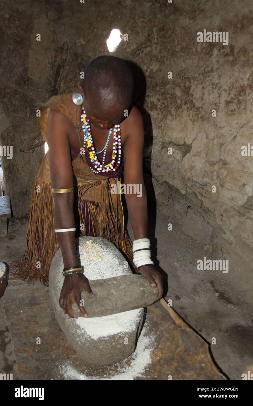 Femme Datoga en cuir traditionnelle robe ornée de perles et de bracelets en laiton la mouture de céréales pour la farine. Banque D'Images