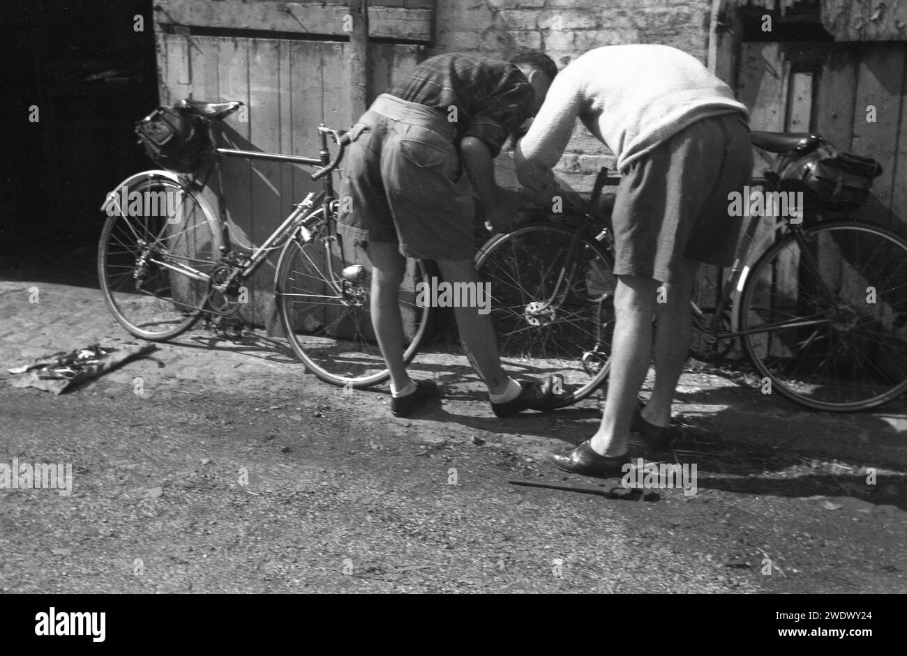 Années 1950, historique, deux cyclistes de tourisme masculins, en short, par leurs vélos contre le mur, avec des outils pour faire quelques réparations, Angleterre, Royaume-Uni. Banque D'Images