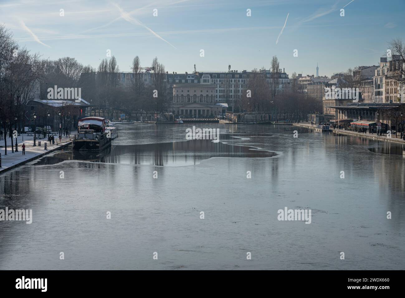 Paris, France - 01 20 2024 : Canal de l'Ourcq. Réflexions sur le canal de l'Ourcq d'immeubles résidentiels, pont, barges et la Rotonde de Stalingrad sur gelé Banque D'Images
