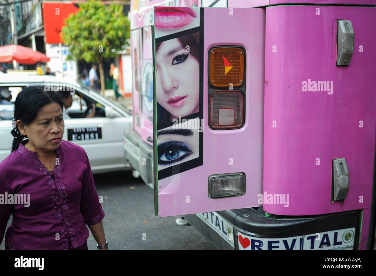 21.02.2014, Yangon, Myanmar, Asien - Eine alltaegliche Strassenszene zeigt eine einheimische Frau, die im Stadtzentrum an einem bus mit Werbung fuer Kosmetik vorbeigeht. *** 21 02 2014, Yangon, Myanmar, Asie une scène de rue quotidienne montre une femme locale marchant devant un bus faisant de la publicité pour des cosmétiques dans le centre-ville Banque D'Images