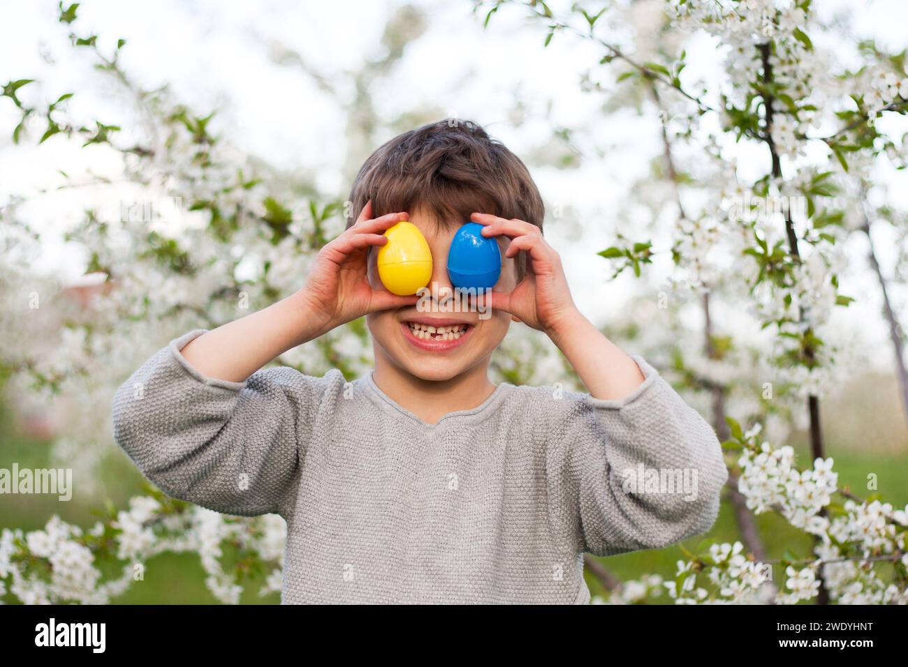 Joyeuses pâques. Mignon garçon drôle d'enfant d'âge préscolaire avec des œufs de Pâques dans le jardin, portrait sur fond d'arbre en fleurs. Enfant riant pendant un œuf de Pâques Banque D'Images