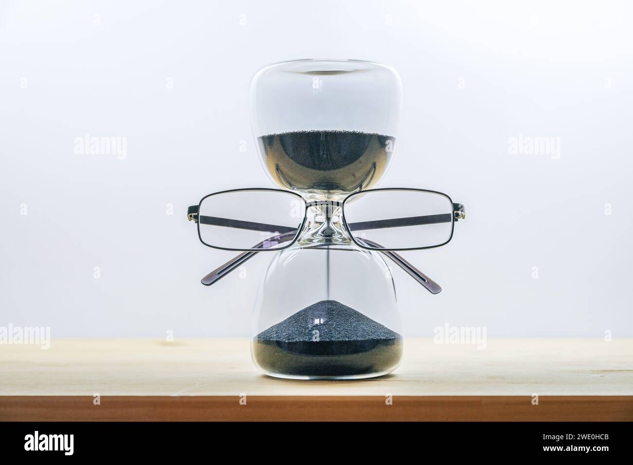 Gardez un œil sur le temps, sablier avec du sable noir portant des lunettes, concept d'entreprise de délai qui s'épuise, table en bois sur un fond gris clair Banque D'Images