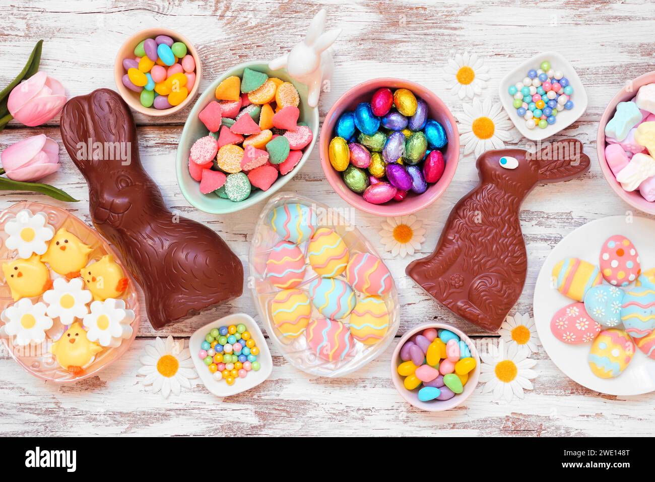 Scène de table de bonbons de Pâques. Vue de haut en bas sur un fond de bois blanc. Lapins en chocolat, œufs de bonbons et une collection de bonbons. Banque D'Images