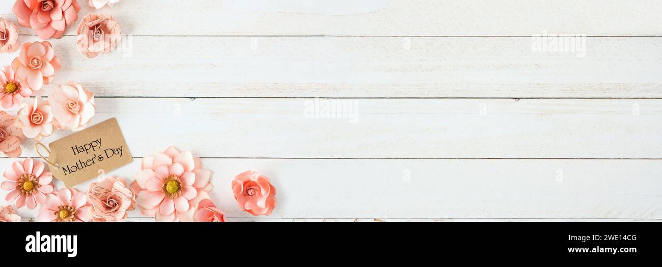 Bordure d'angle Happy Mothers Day avec fleurs en papier rose et étiquette cadeau. Vue de dessus contre un fond de bannière en bois blanc. Espace de copie. Banque D'Images