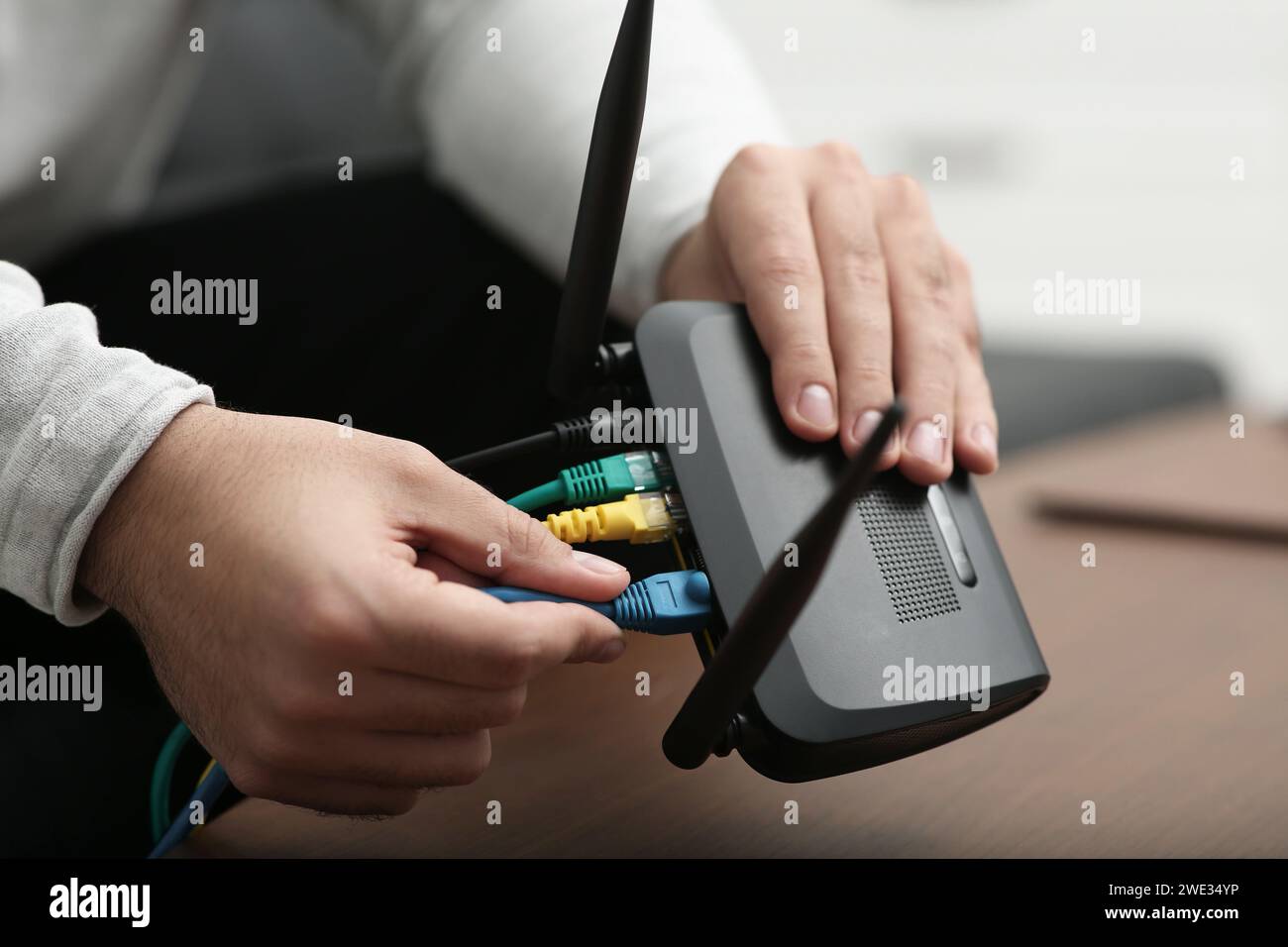Homme insérant le câble dans le routeur Wi-Fi à la table en bois à l'intérieur, gros plan Banque D'Images