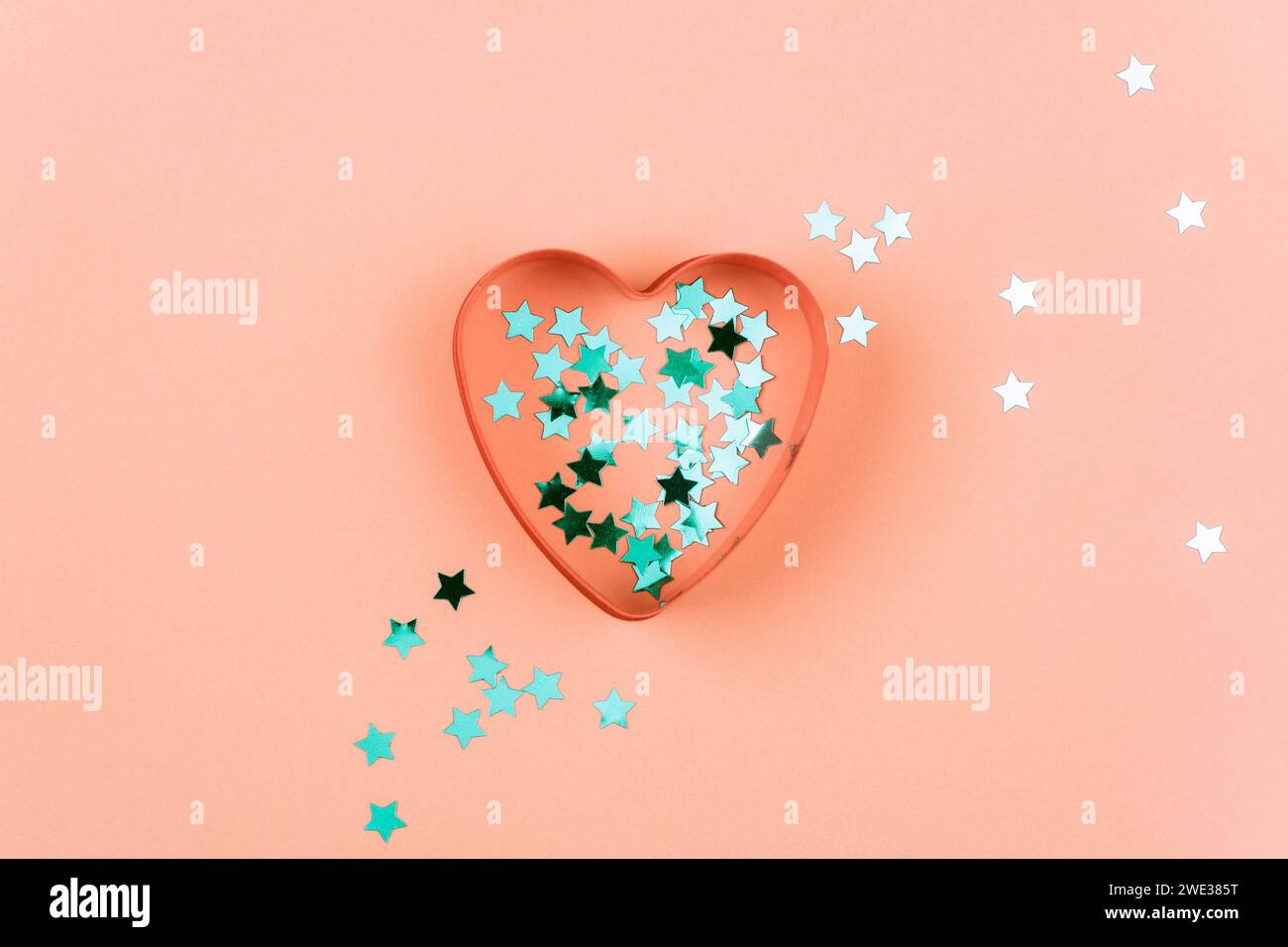 Emporte-pièce en forme de coeur et confettis bleus sur fond rose corail. Concept de Saint Valentin. Vue de dessus, pose à plat. Banque D'Images