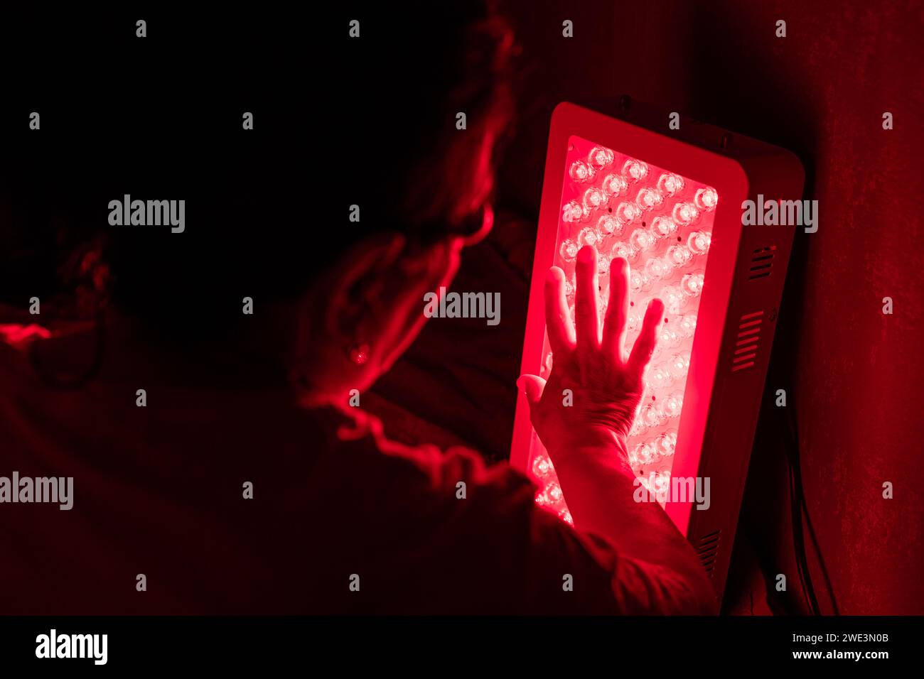 Gros plan de la femme âgée touchant les LED du panneau de thérapie de lumière rouge avec la main Banque D'Images