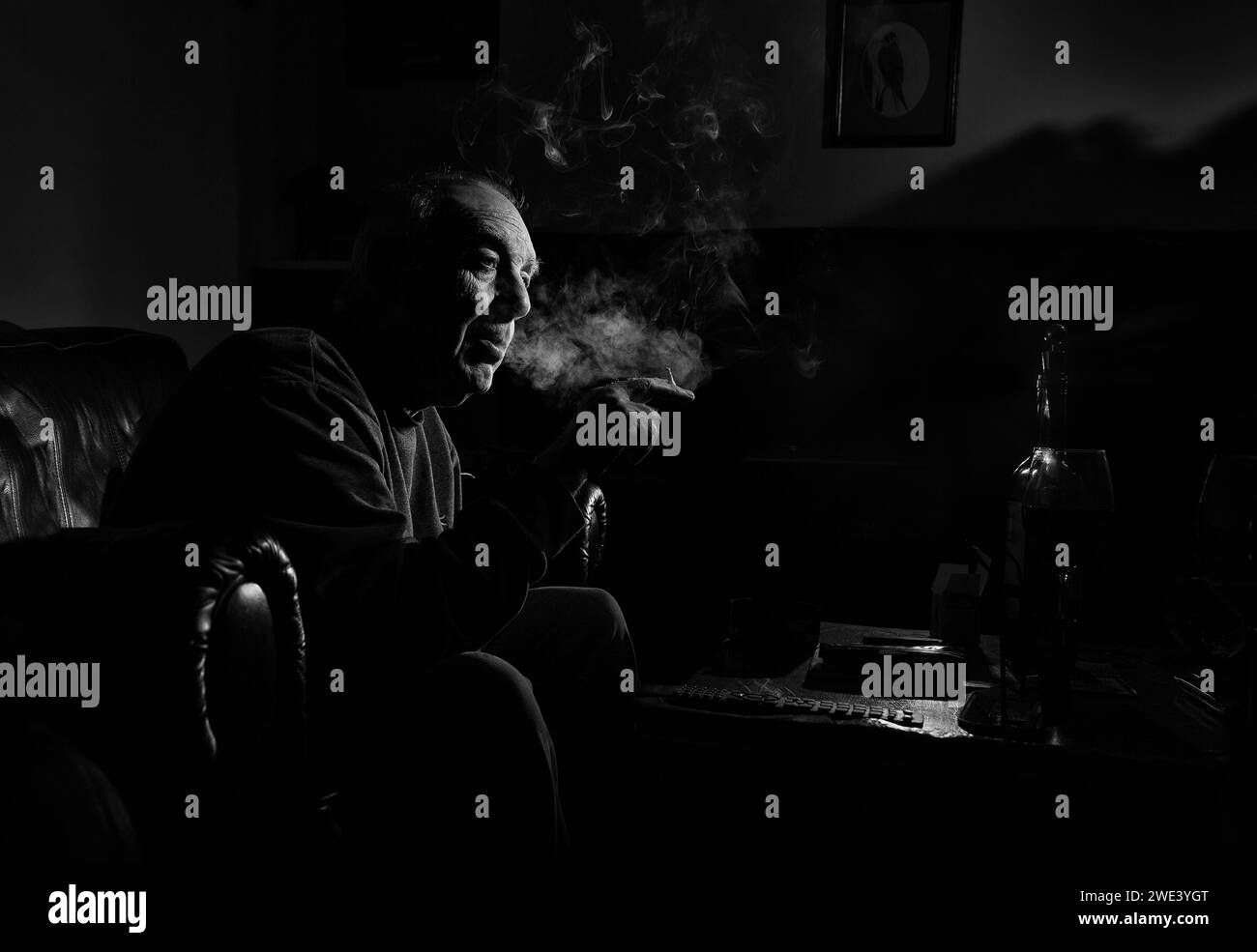 Un homme fumant une cigérette roulée dans une chambre noire Banque D'Images
