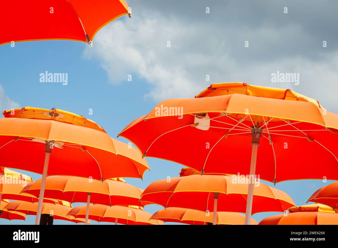Fond d'été. Vue à angle bas des parasols orange contre le ciel bleu et les nuages. Banque D'Images