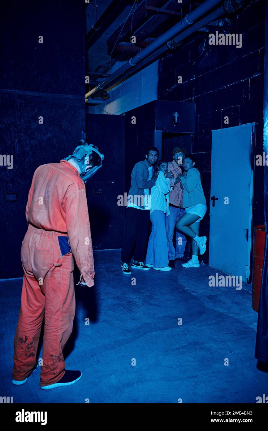 homme dans le mât de gaz debout près du groupe multiculturel effrayé de personnes dans la salle d'évasion, aventure de quête Banque D'Images